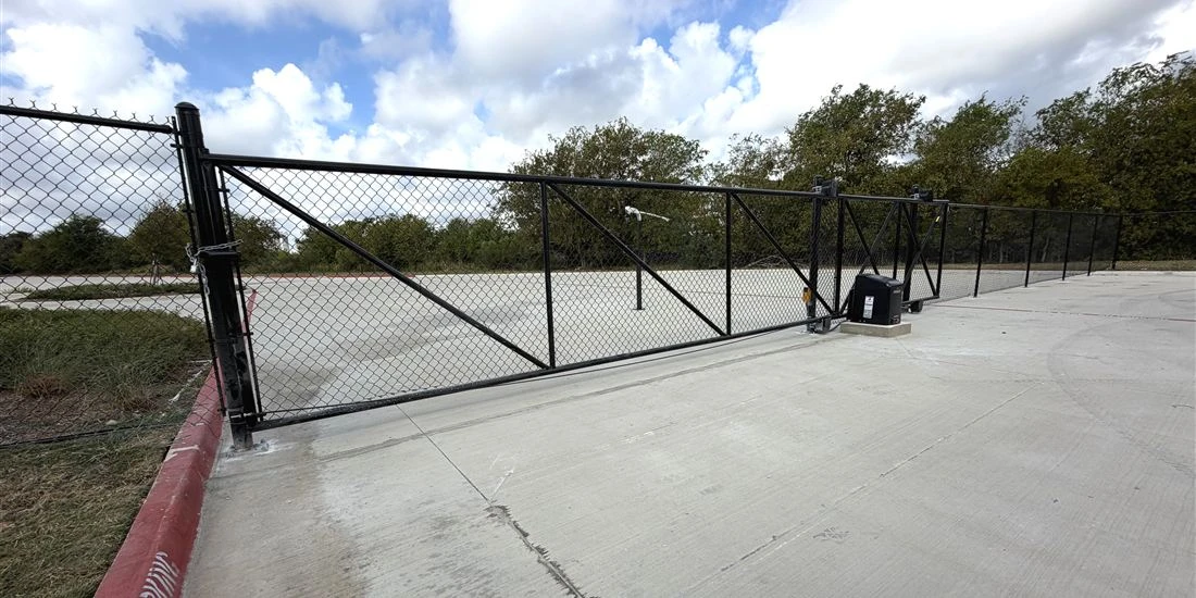 Black chain link cantilever gate with an automatic gate operator at a commercial facility in New Braunfels, Texas