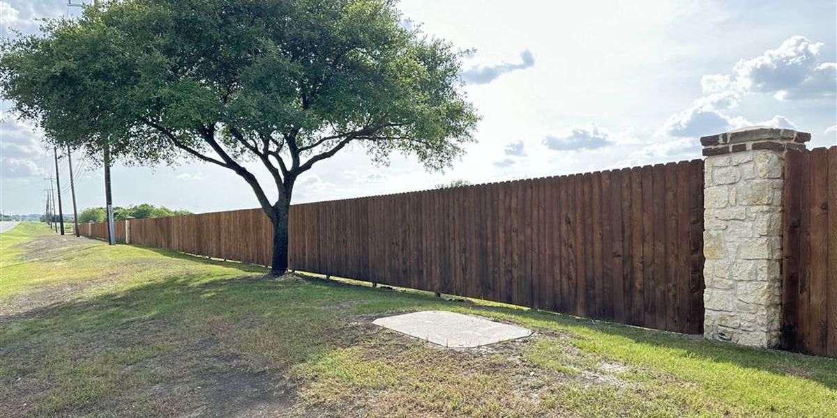 Long stained wood privacy fence with stone column along a roadway