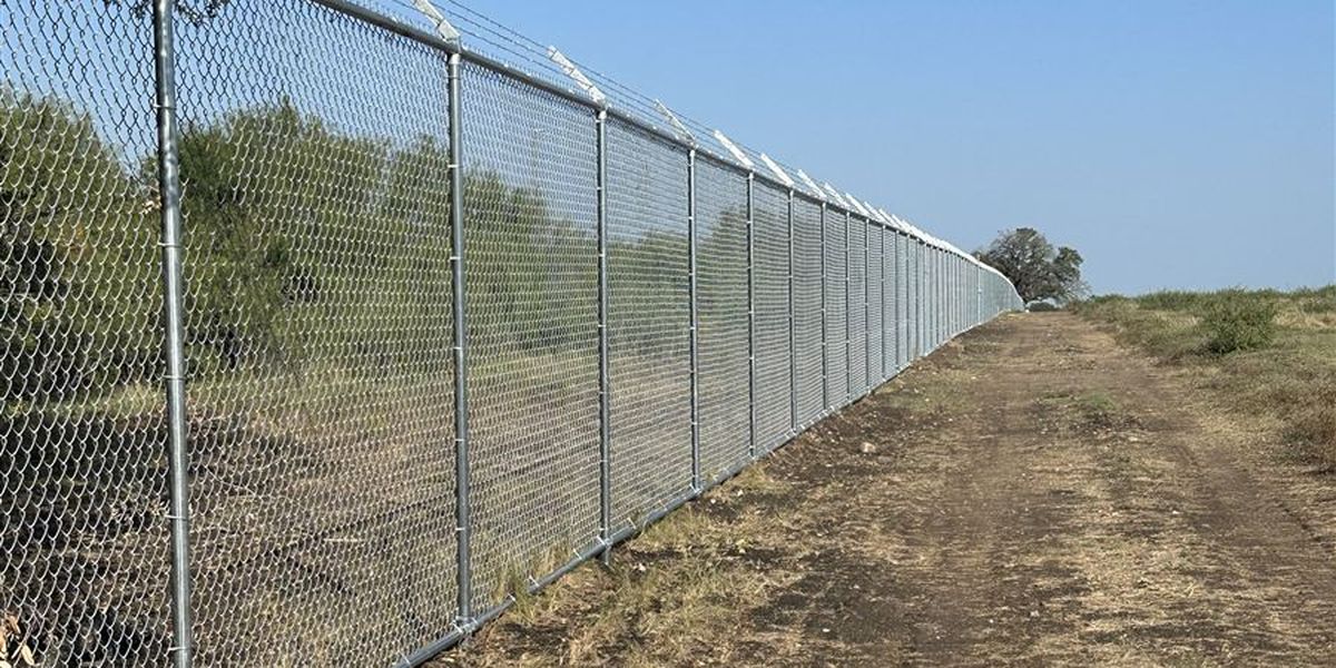 Long run of new chain link perimeter fence with barbed wire arms